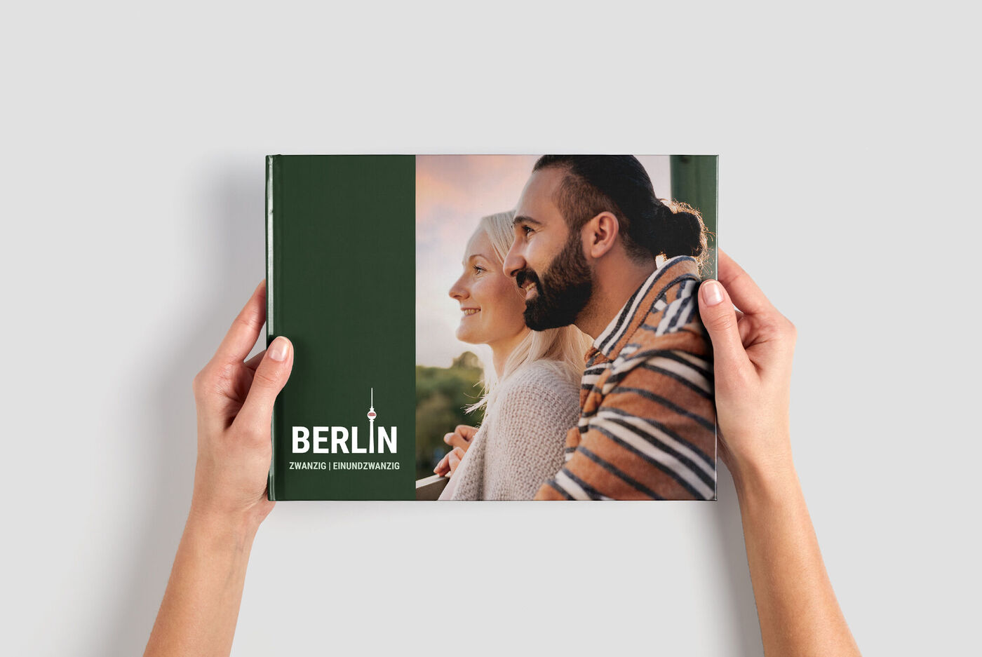 Iemand houdt een CEWE FOTOBUCH vast met een groene cover en de tekst 'Berlijn'.
